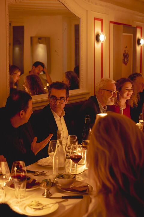 Deux convives en pleine discussion à table pendant le dîner d’Espèces d’espaces, sous un grand miroir et des appliques allumées.
